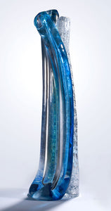 A tall hand blown glass sculpture featuring layers of blue, silver, and clear glass stands against a white background.