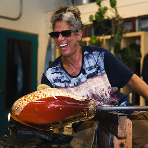 Vermont based glassblower Randi Solin smiles while creating a handblown vessel in her Brattleboro glassblowing studio.