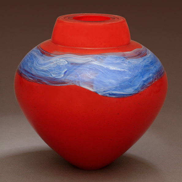 A bright red blown glass vessel with a band of silver blue glass stands against a gray background.