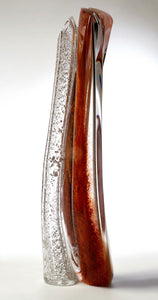 A tall hand blown glass sculpture featuring layers of red and silver in thick clear glass stands against a white background.
