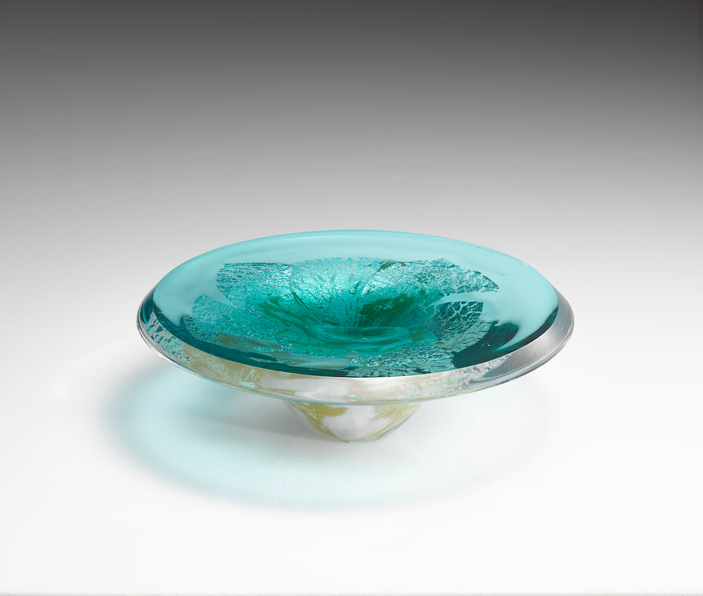 A thick blue translucent hand blown glass platter features layers of silver foil within clear glass.