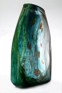 A sculptural blown glass vessel featuring blue, green, and clear glass stands against a white background.