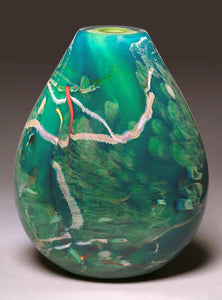 A hand blown glass vessel featuring layers of aquatic blues, greens, and veins of white glass stands against a light gray background.