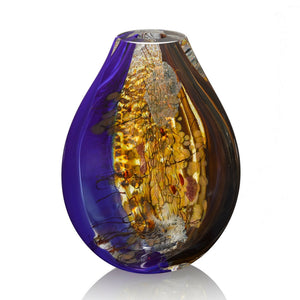 A hand blown glass vessel features layers of brilliant lapis blue, deep chocolate brown, gold aventurine, and shimmering silver leaf encased in thick clear glass.