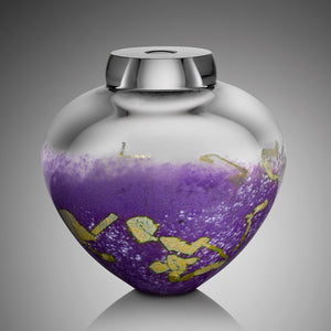 A thick clear hand blown glass vessel features vibrant purple glass on its bottom half, dotted with flecks of silver leaf.