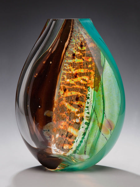 A hand blown glass vessel featuring deep brown, silver, and turquoise glass against a gray background.