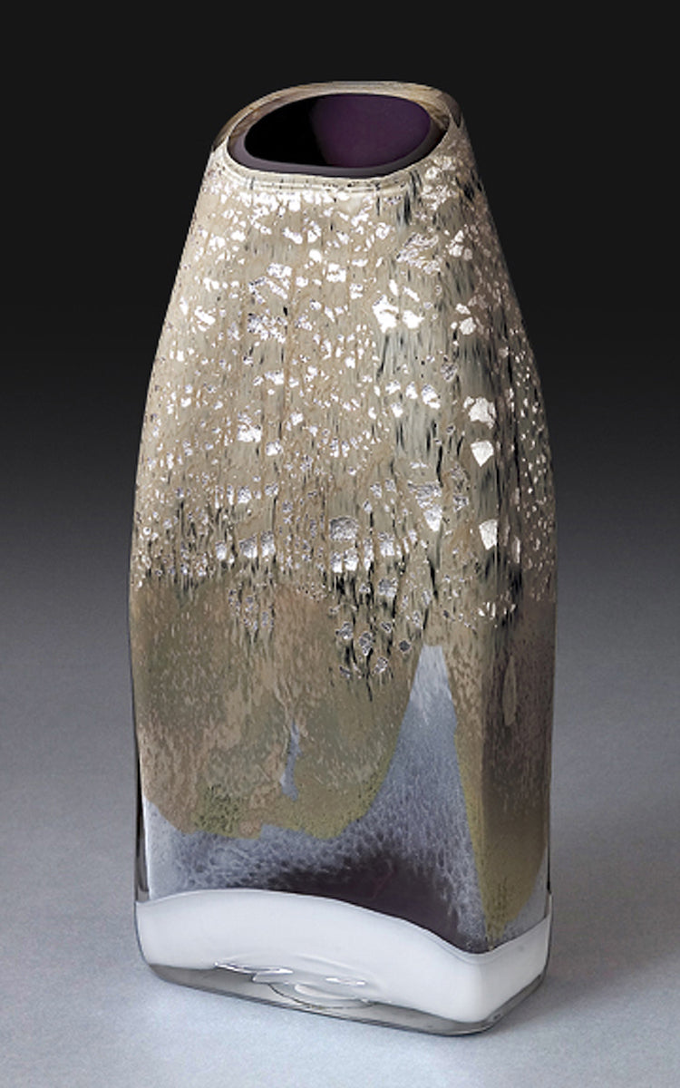 A tall rectangular blown glass vessel featuring shimmering silver leaf stands against a dark gray background