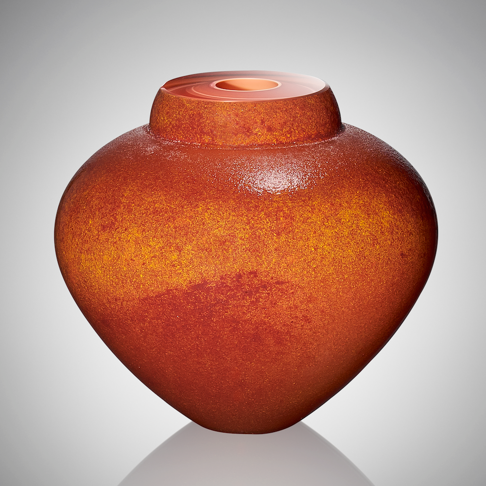 A hand blown glass vessel featuring lightly textured layers of orange, yellow, red, and apricot glasses to evoke the colors of a seashell.